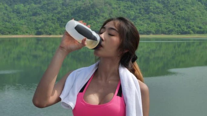 穿着运动服的亚洲美女慢动作视频剪辑慢跑后从瓶子里喝水。早上在自然。健康运动理念