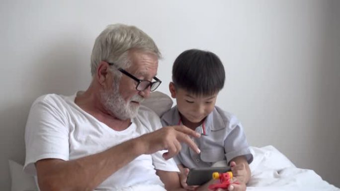 快乐男孩孙子教老年老人祖父在养老院的床上用智能手机玩游戏