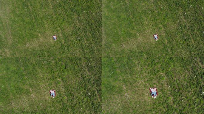 幸福的年轻夫妇躺在草地上。摄像机慢慢飞向他们。空中自上而下。4K