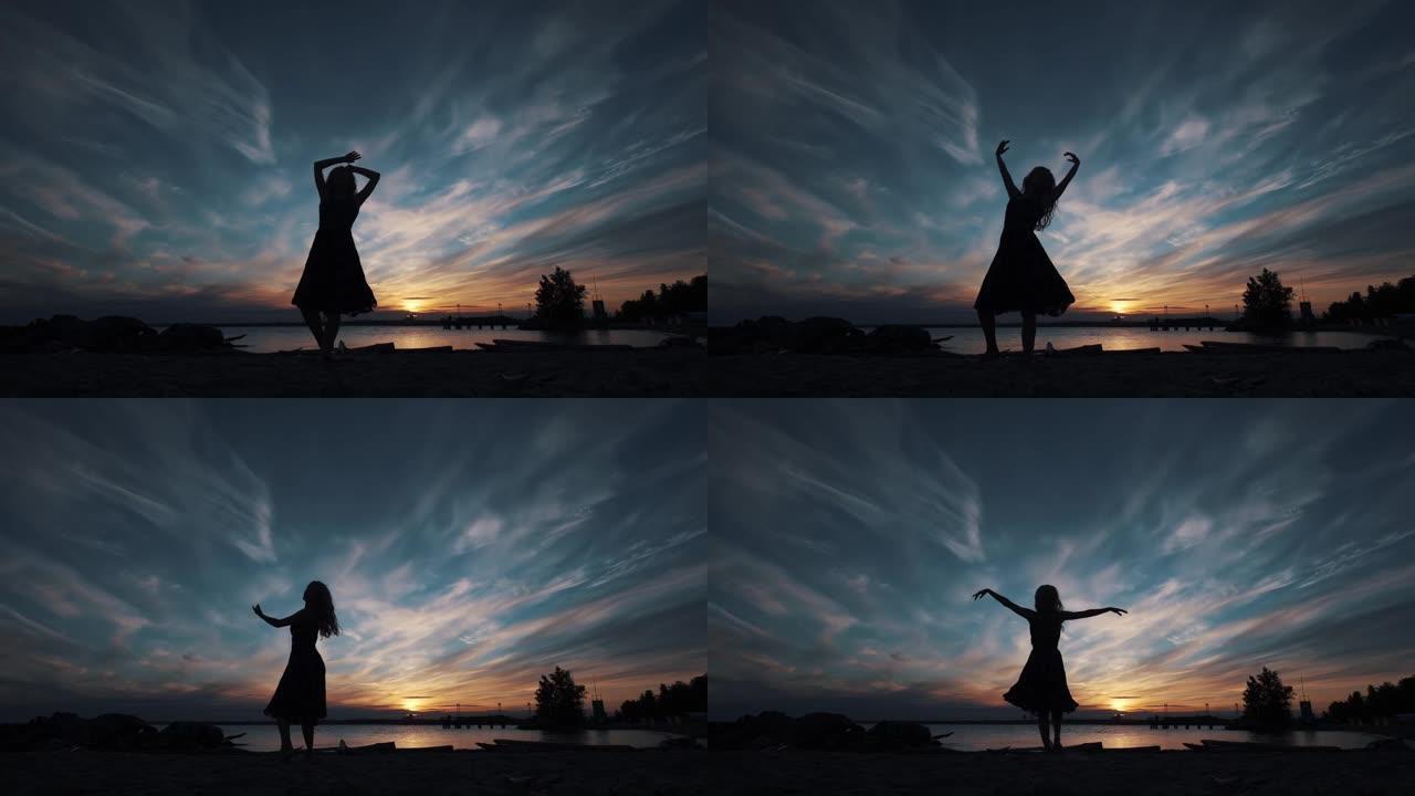 年轻女孩在日落的背景下优雅地跳舞。穿着飞行连衣裙的芭蕾舞演员的轮廓。