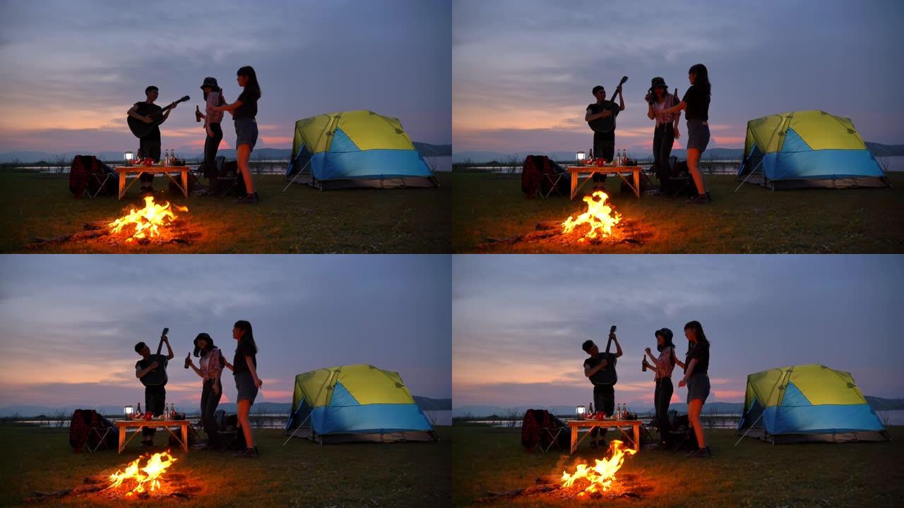 场景慢动作亚洲青少年群体在篝火帐篷前一起享受，在暑假期间在湖边观赏日落。他们在假期、放松的时刻快乐、