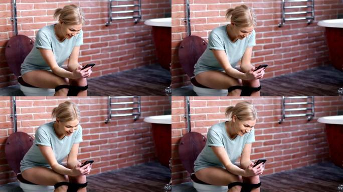 国内年轻女子微笑着用智能手机坐在家里浴室的马桶上