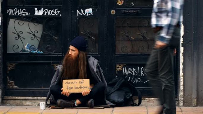 无家可归的人拿着 “底部” 的纸板，在拥挤的街道上乞讨