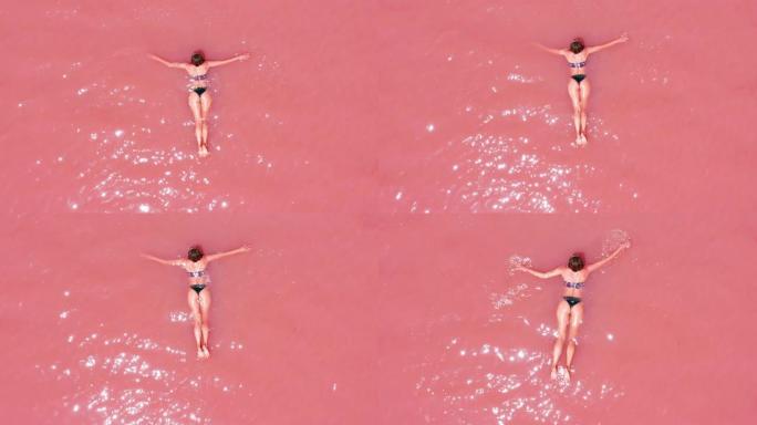 鸟瞰图。一个美丽的年轻女孩躺在粉红色的湖上，比基尼，太阳镜，粉红色的清澈的水，俯视图。概念: 海上空