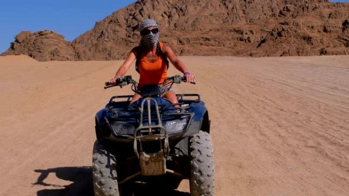 骑四轮摩托的女孩在群山背景下穿越埃及的沙漠