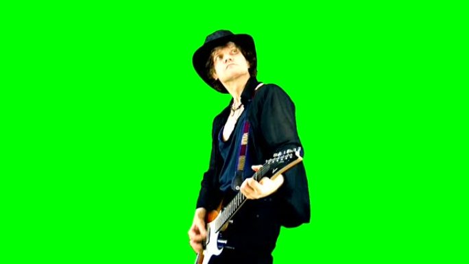 戴着帽子的酷摇滚吉他手在色键上弹奏电吉他。音乐家在绿色背景下表演。