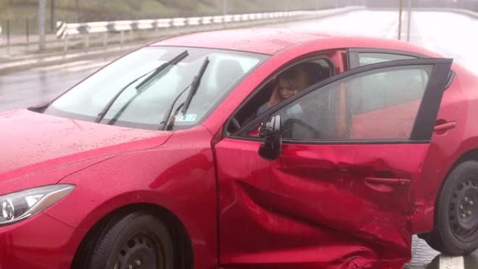 一个女孩在雨中潮湿的道路上发生车祸后坐在一辆破车里。