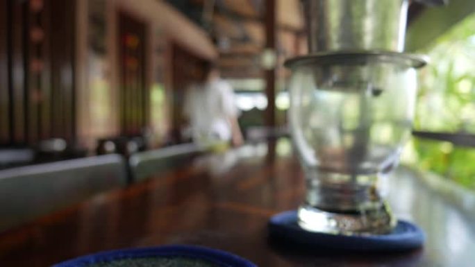 顾客在咖啡馆喝冰茶等待使用越南传统的phin过滤器酿造黑咖啡。咖啡在玻璃杯中慢慢滴落。Ca phe 