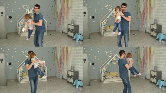 戴着眼镜的年轻父亲抱着2岁的小女儿在家里的孩子房间里旋转。