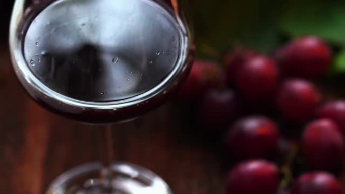 慢动作剪辑，将红酒滴在水晶玻璃杯中，有机新鲜葡萄和背景上的空瓶，最好的饮料理念，免费的文本空间。