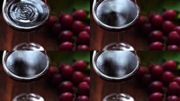 慢动作剪辑，将红酒滴在水晶玻璃杯中，有机新鲜葡萄和背景上的空瓶，最好的饮料理念，免费的文本空间。