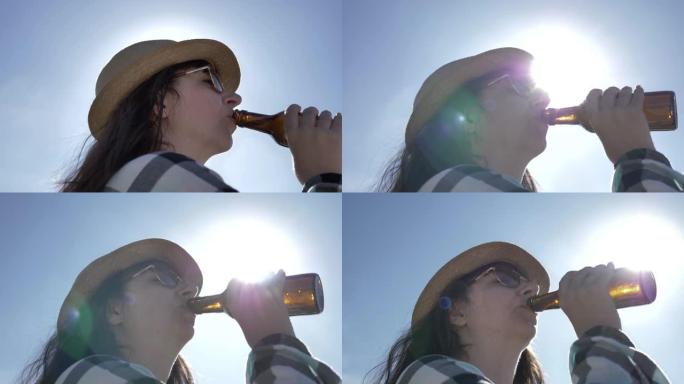戴着帽子和太阳镜的女人在阳光明媚的天空的背景下喝啤酒