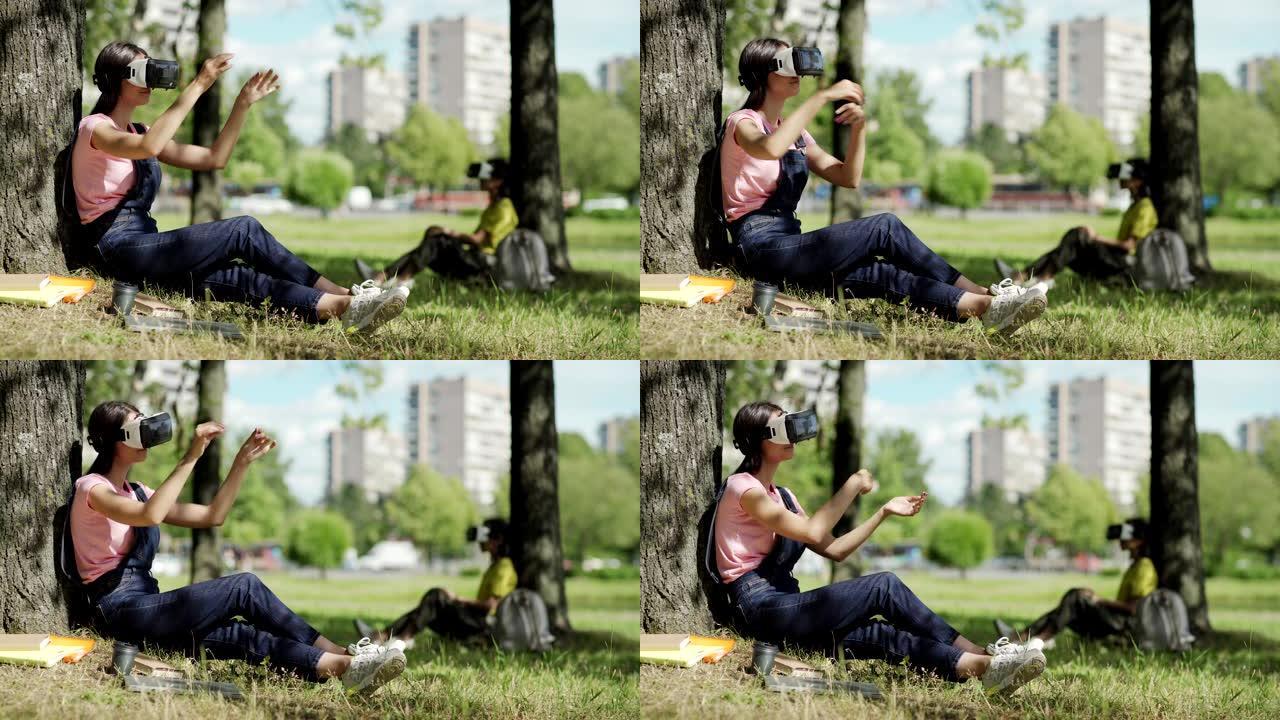 VR耳机中女学生的侧视图在公园的树下滑动可视化数据。另一个在背景中戴着虚拟现实眼镜的女大学生