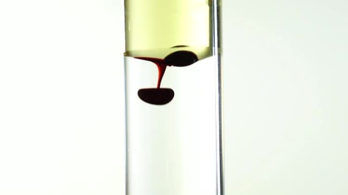在透明试管中，红色食品彩色墨水从油中滴入水中的视频片段，特写