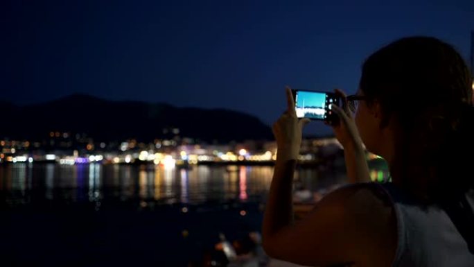 一名年轻女子通过电话拍摄克里特岛的夜海岸