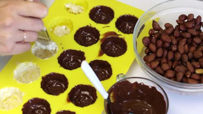 一名妇女涂抹硅胶模具，用融化的白巧克力制成巧克力上釉的糖果。用刷子。附近有杏仁填充