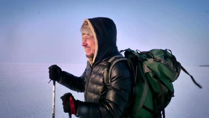 穿着疲惫的背包客的肖像，带着山棍和巨大的袋子，艰难地沿着雪域行走。