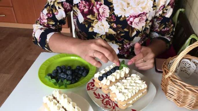 一个女人用薄荷叶装饰蛋糕。多层的savoiardi饼干和奶油层用蓝莓装饰。