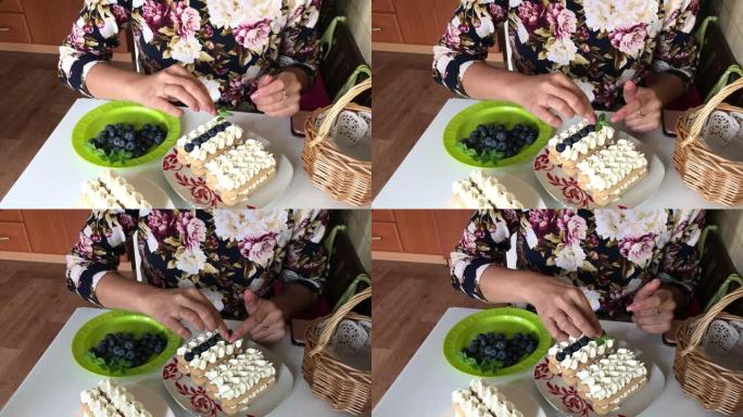 一个女人用薄荷叶装饰蛋糕。多层的savoiardi饼干和奶油层用蓝莓装饰。