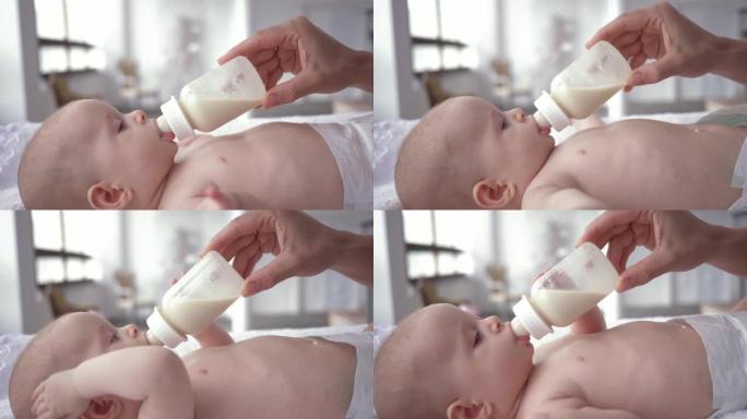 女婴从母亲手中拿着的瓶子里喝牛奶的肖像，尿布中的新生儿躺在换衣桌上特写