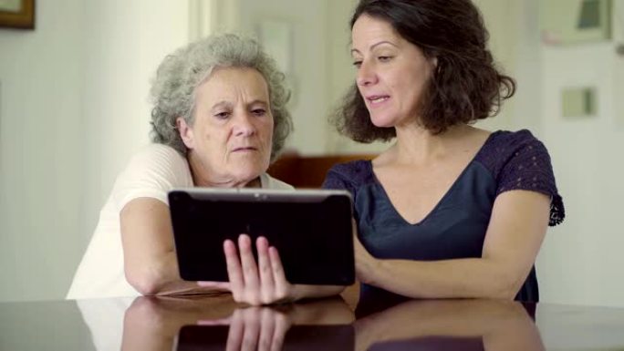 两个女人坐在桌旁使用平板电脑。