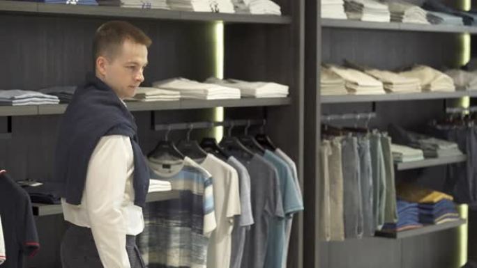 一个英俊的男人在男性服装精品店的陈列室里展示白色时尚衬衫。多种选择。品牌男装精品