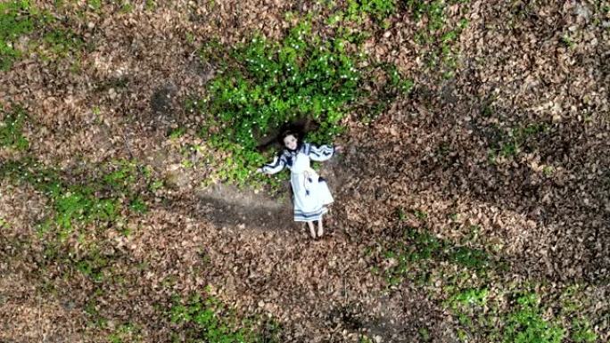 顶部的鸟瞰图。一个小女孩闭着眼睛躺在白花的草地上。摄像机慢慢移开并接近。从无人机拍摄