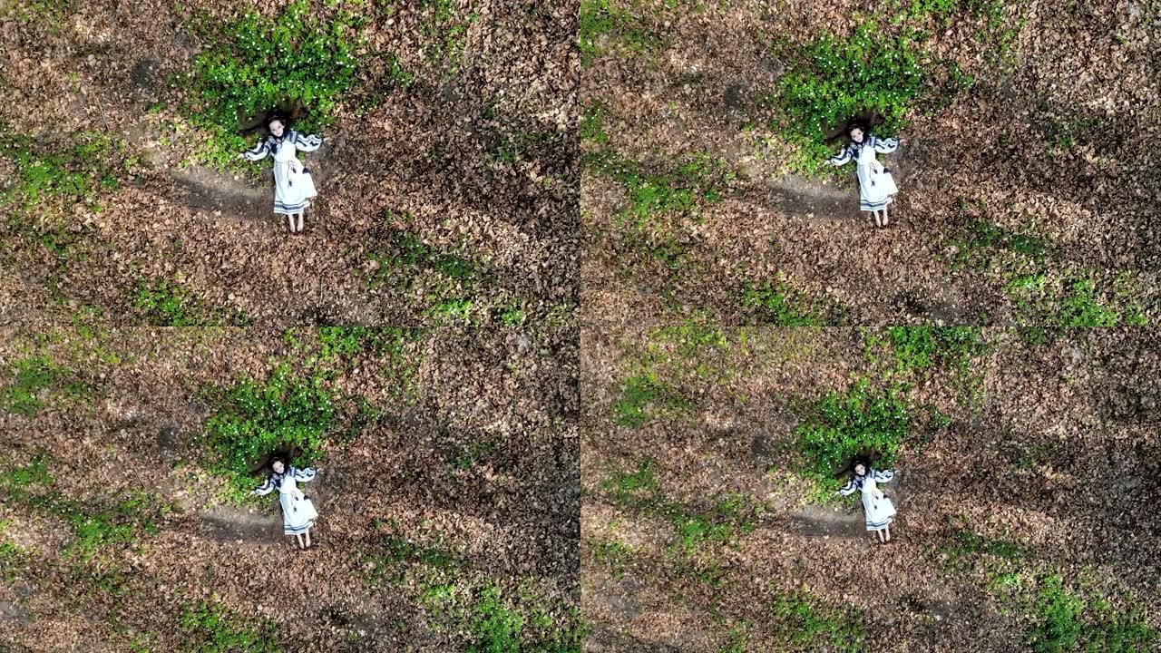顶部的鸟瞰图。一个小女孩闭着眼睛躺在白花的草地上。摄像机慢慢移开并接近。从无人机拍摄