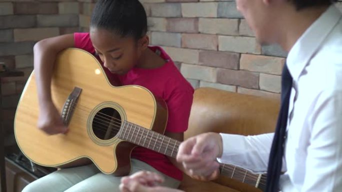 年轻的亚洲男教师给吉他课和教如何弹吉他的非洲裔美国女孩