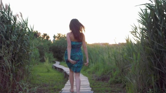 快乐迷人的女孩赤脚在木桥上奔跑，在日落时在高绿草丛中享受自然