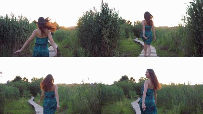 快乐迷人的女孩赤脚在木桥上奔跑，在日落时在高绿草丛中享受自然