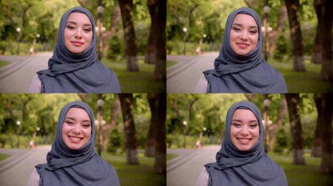 戴着头巾的穆斯林妇女的肖像，明亮的化妆害羞地微笑着，快乐地走进公园里的相机。