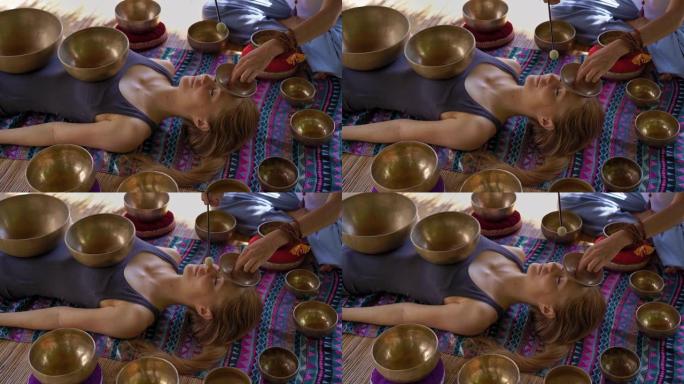 一位亚洲神圣医学大师的超级镜头为一位年轻女性表演了藏族碗治疗仪式。用藏族歌唱碗冥想。他们在凉亭里冥想