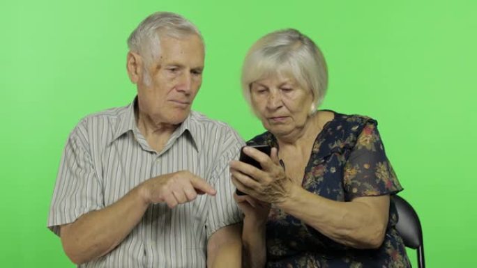 老年男女坐在一起，在智能手机上工作。色度键