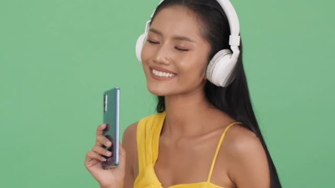 亚洲美女在线听音乐快乐情感微笑。戴着耳机和手持智能手机的女人。美丽、时尚和音乐体验的概念。