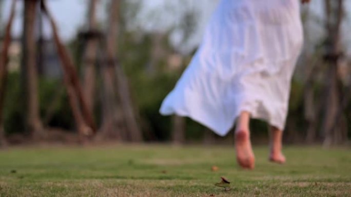 穿着白色新娘礼服的跑步女人，赤脚在草地上跑步，超级慢动作，低角度和后视，慢慢跑出焦点。