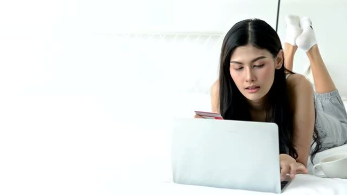 微笑的年轻女子拿着黄金Visa信用卡，看着笔记本电脑在网上购物