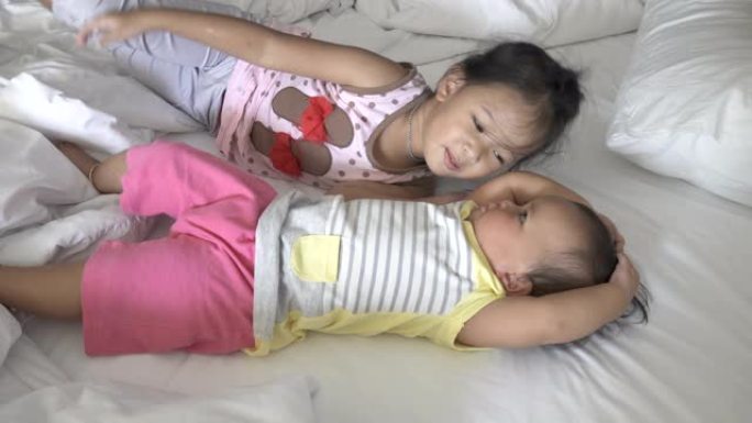 大姐姐亲吻她的孩子，表达爱意。躺在床上的亚洲女孩。叫醒躺在床上的姐妹们。