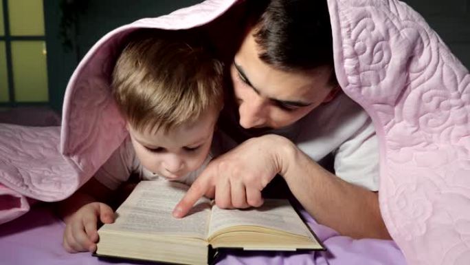 爸爸教他的小儿子读一本藏在毯子下的书。