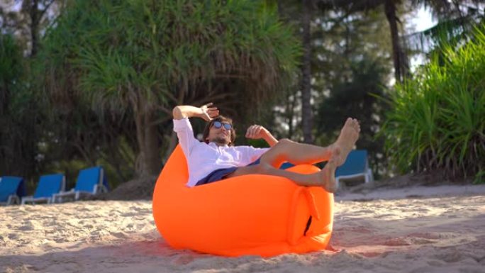 热带海滩上的年轻人躺在刚刚充气的充气沙发上。暑假概念