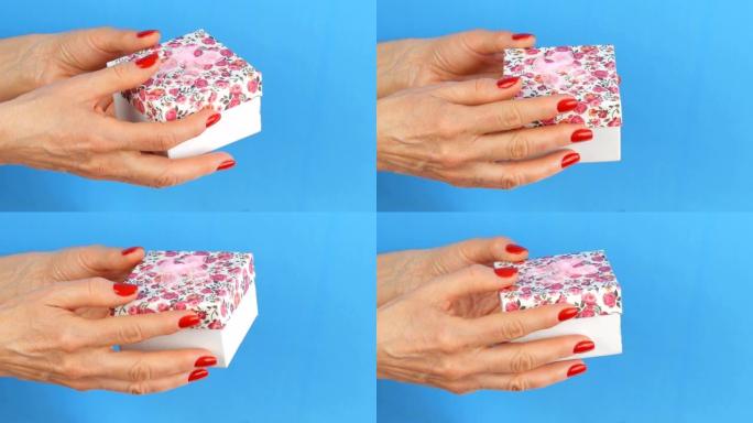 一个带有花卉图案和粉红色蝴蝶结的小礼品盒，由指甲涂有红色指甲油的女人的手握住