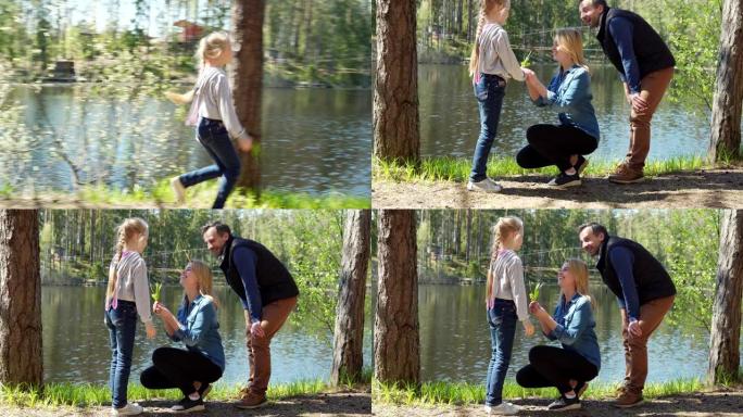 开朗的小女儿跳着父母站在乡下湖边，给幸福的母亲一小束绿草和鲜花。家庭在大自然中快乐地交谈