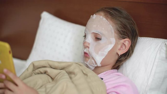 年轻女孩用布化妆品面膜在皮肤脸上躺着不好。十几岁的女孩使用智能手机，而化妆品面膜在家里。问题皮肤护理
