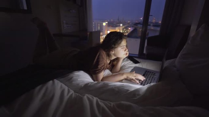 在暮光之城的床上在笔记本电脑上工作的女人
