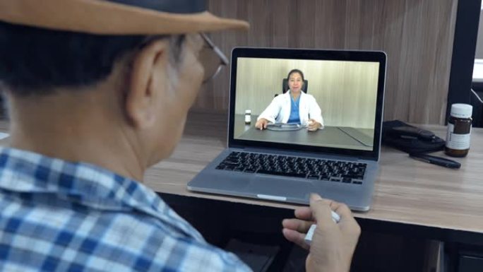老年亚洲男性患者正在通过在家中使用笔记本电脑与女医生交谈，家庭保健概念高级，女医生建议在家中老年患者