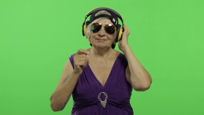 老年妇女戴着耳机听音乐，跳舞。祖母。色度键