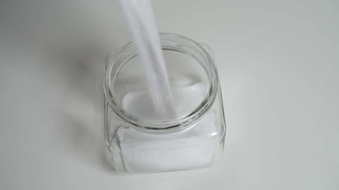 慢慢地将盐倒入站在白色桌子上的玻璃罐中