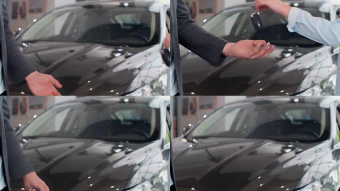 Famale hand在汽车经销店附近给男手提供了车钥匙。无法识别的汽车销售商和一个买了车的女人握手