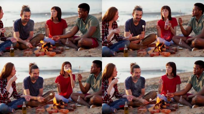 跟踪四个不同的年轻朋友在海滩篝火旁放松，聊天，烧烤，吃棉花糖和喝啤酒的左中景
