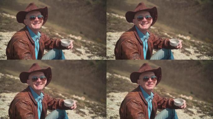 在山上，一个男人戴着牛仔帽，皮夹克，蓝色牛仔裤和眼镜。男人看着镜框笑了。